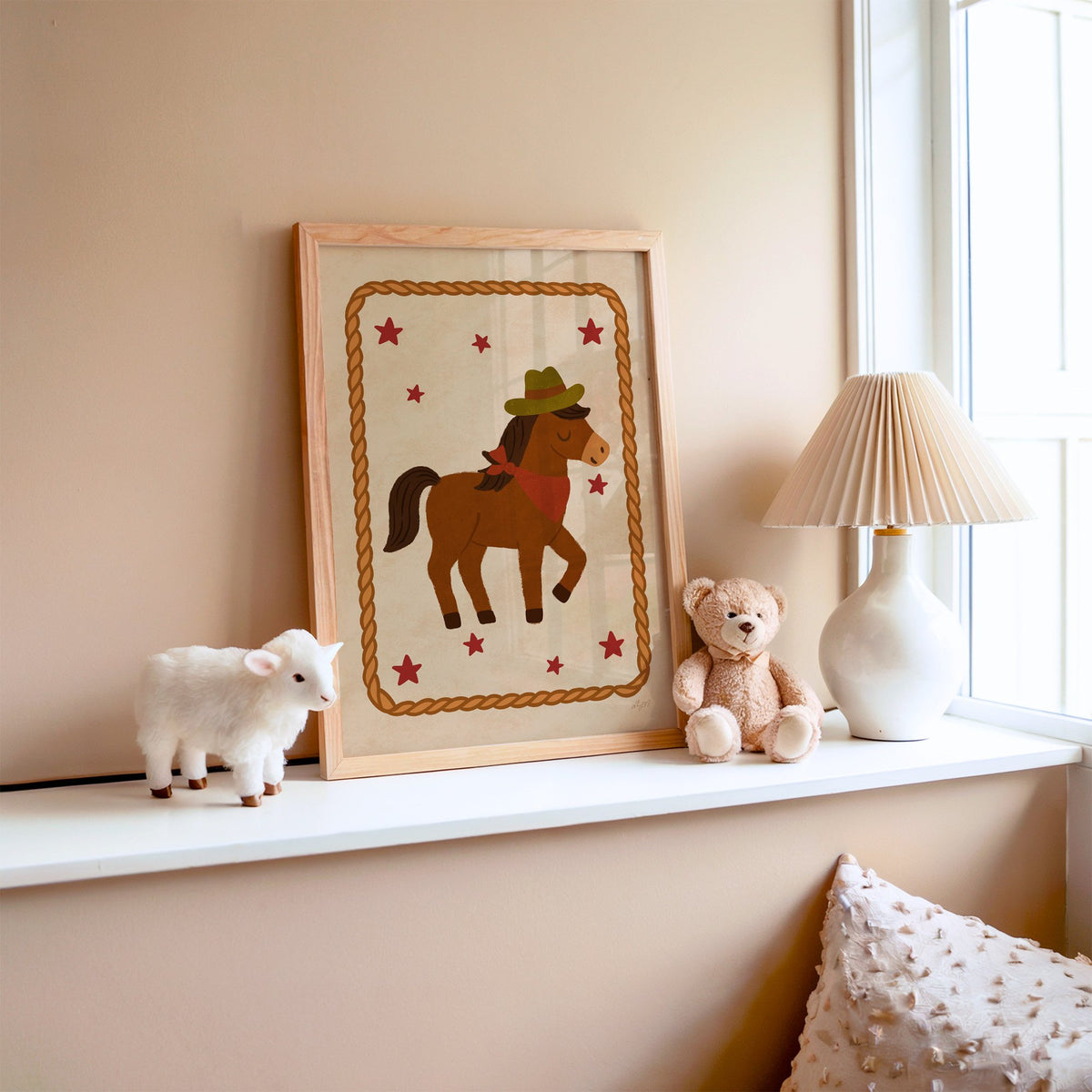 Cowboy pony in rope frame nursery print in an oak frame on a window ledge with a toy lamb and teddy
