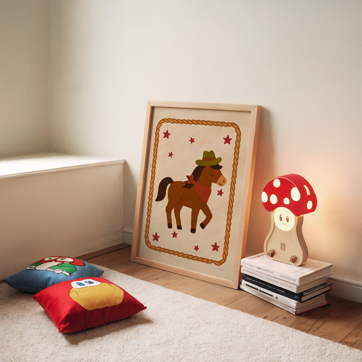 Cowboy pony in rope frame nursery print in an oak frame leaning on a rug beside a mushroom lamp and floor cushions