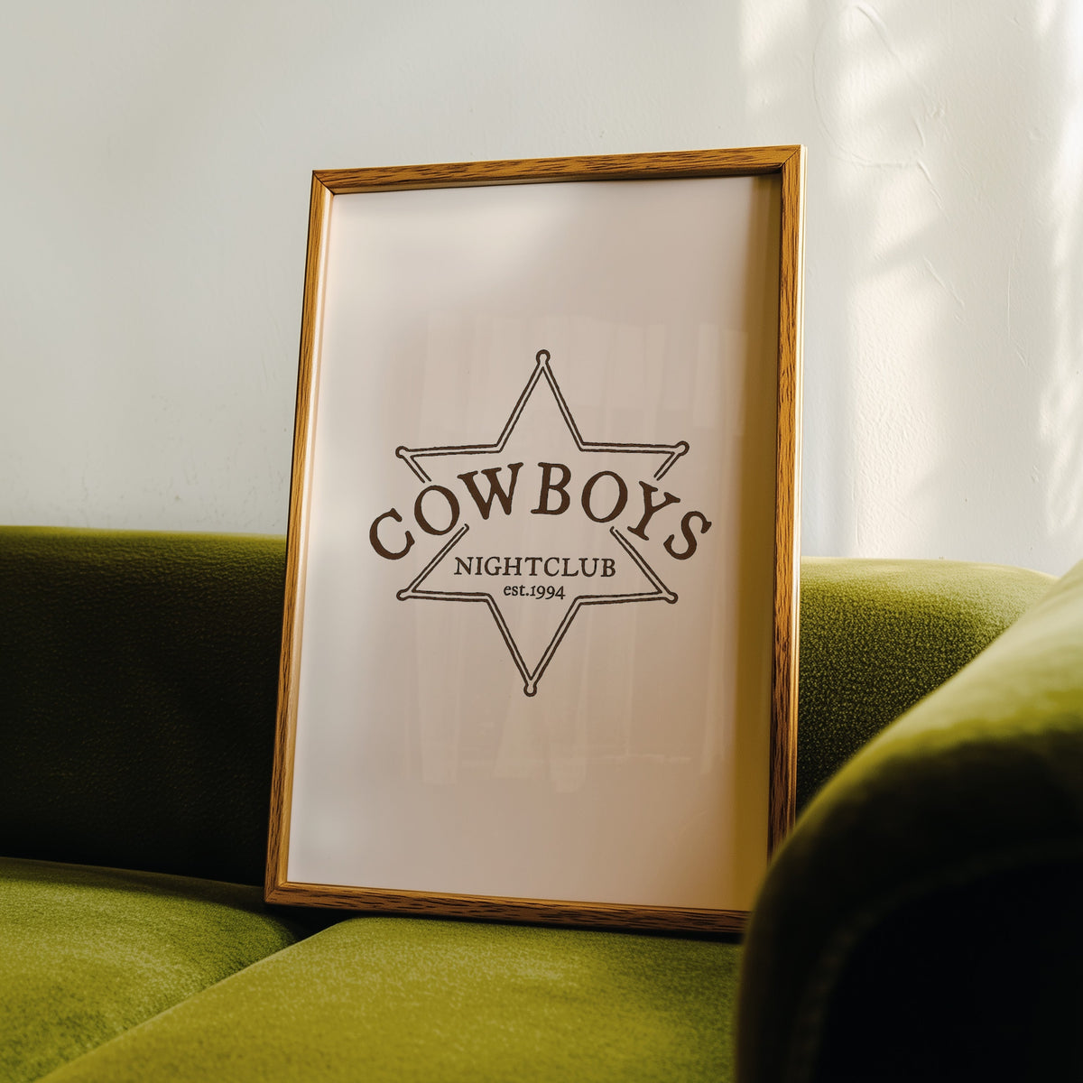 Cowboys Nightclub star print in an oak frame leaning on a green velvet sofa