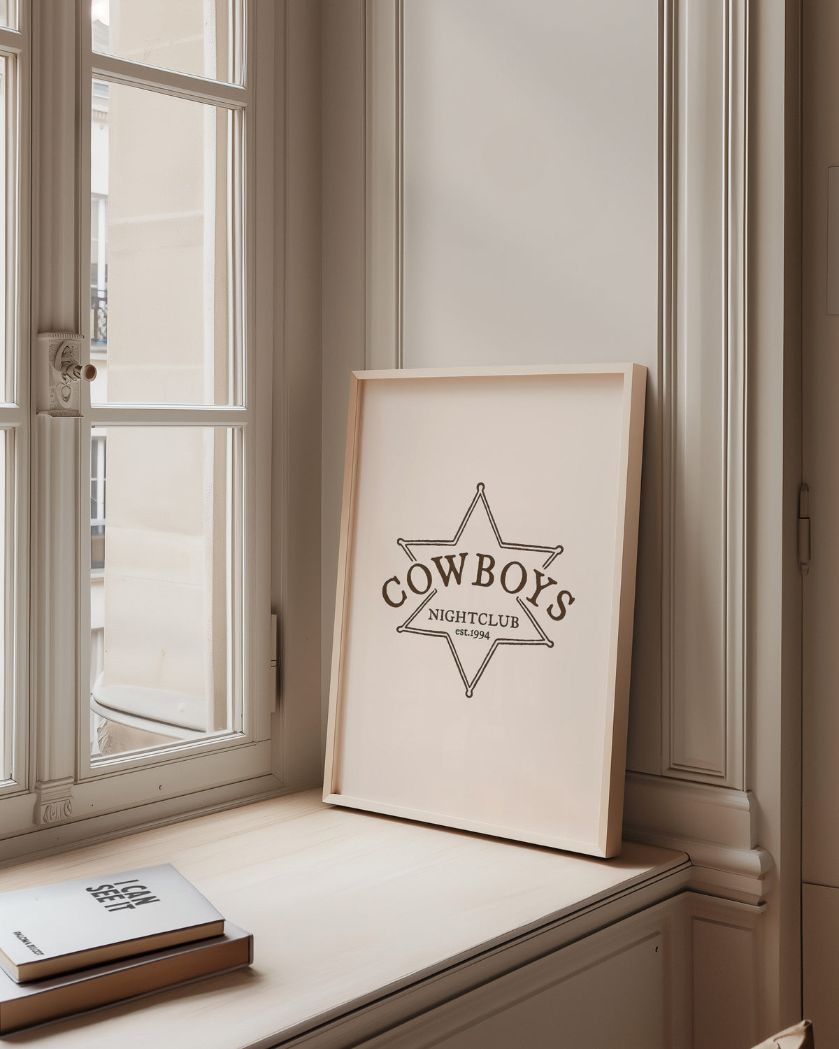 Cowboys Nightclub star print in a pale wood frame on a sunlit window ledge