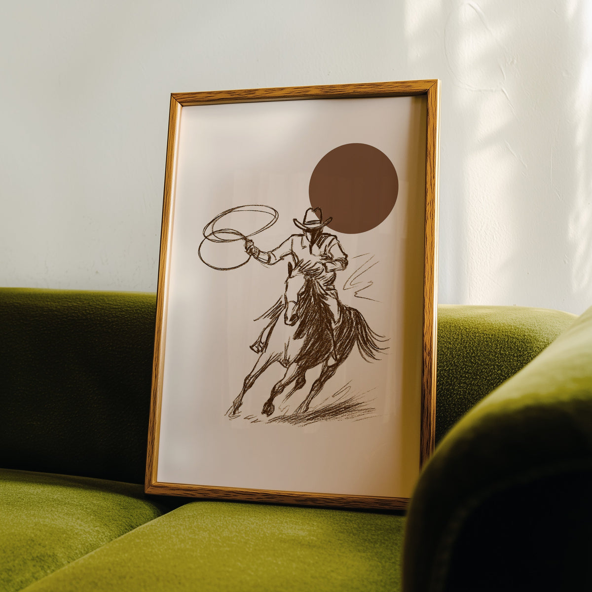Cowgirl galloping horse print in an oak frame leaning on a green velvet sofa