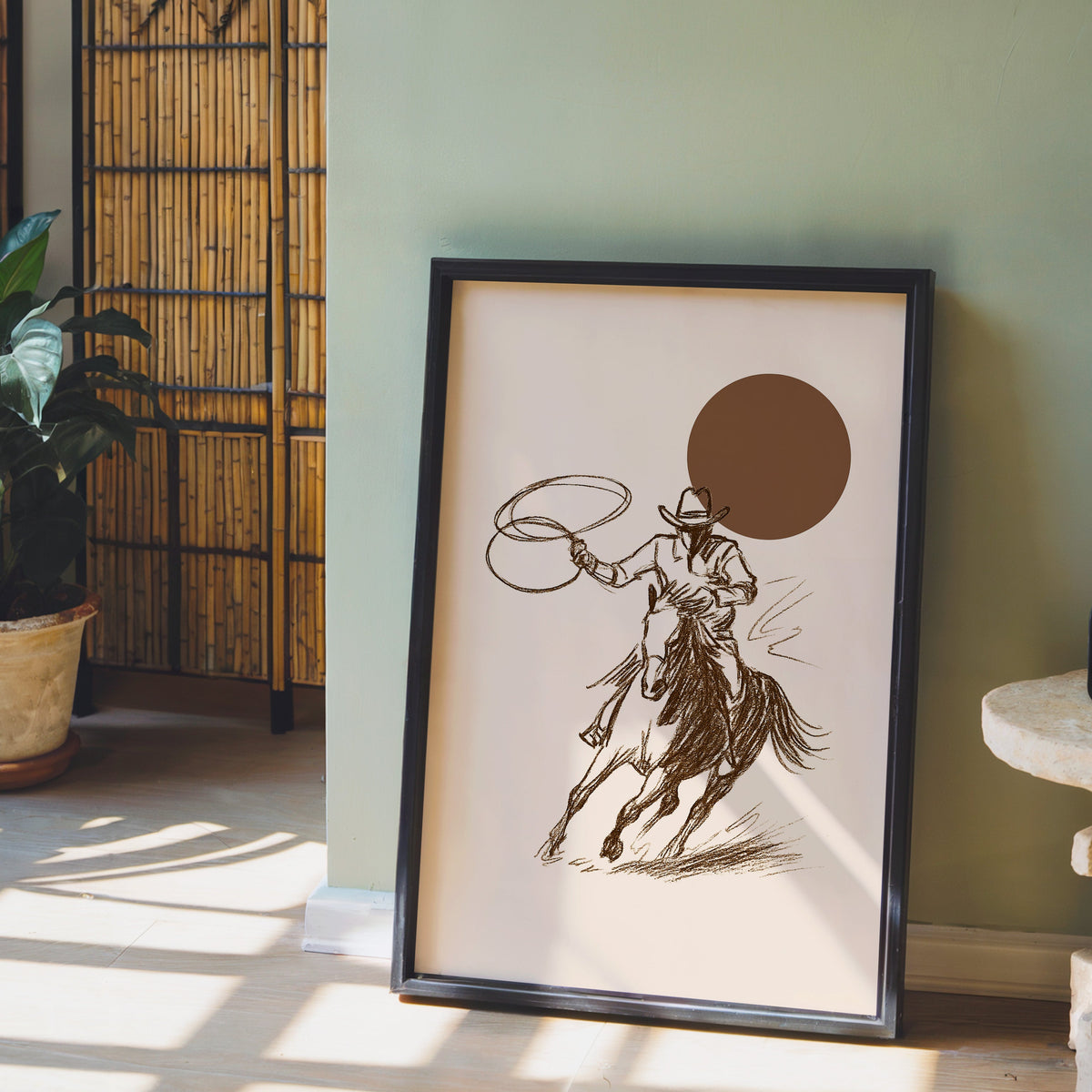 Cowgirl galloping horse print in a black frame leaning against a sage green wall