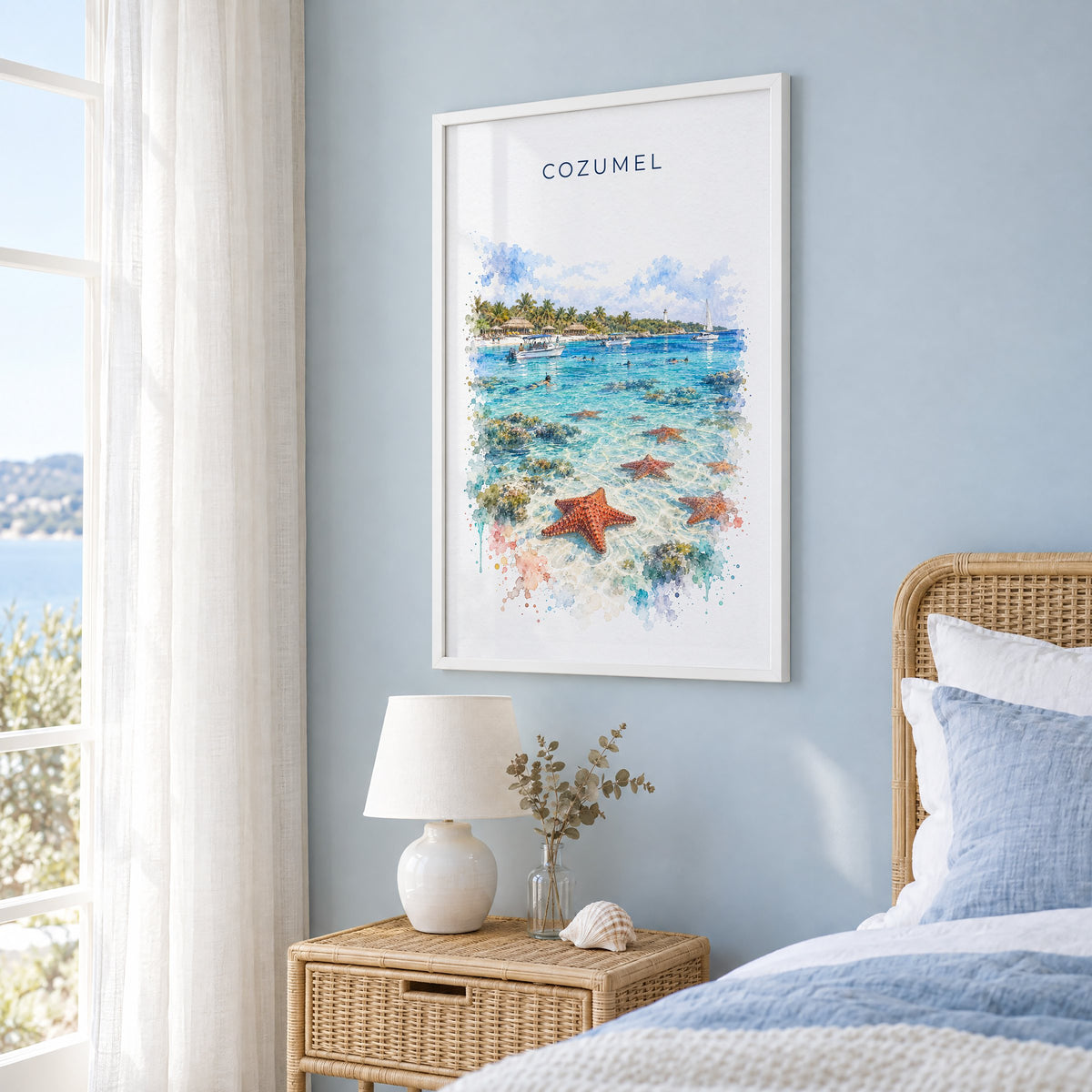 Cozumel watercolor print in a white frame on a pale blue wall beside a rattan bed in a coastal bedroom