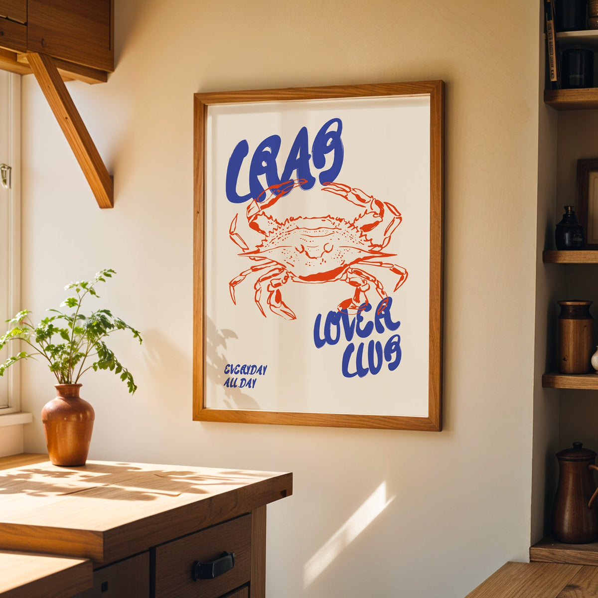 Red line crab print in a wood frame on a sunlit kitchen wall beside open shelving
