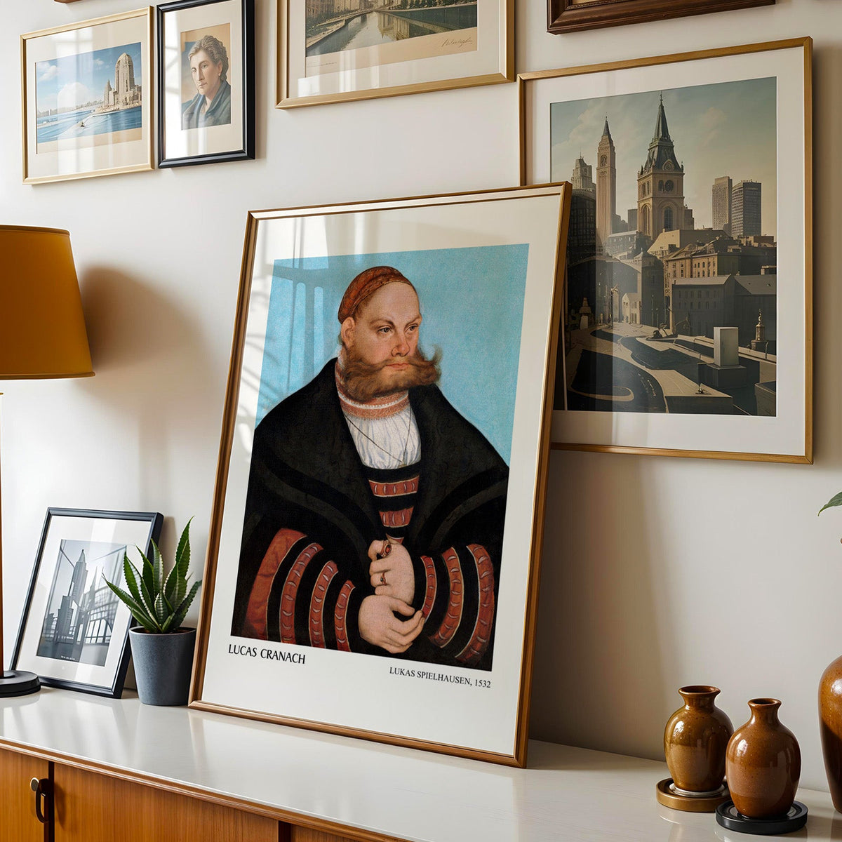 German portrait print shown in a gold frame leaning on a sideboard in a gallery wall