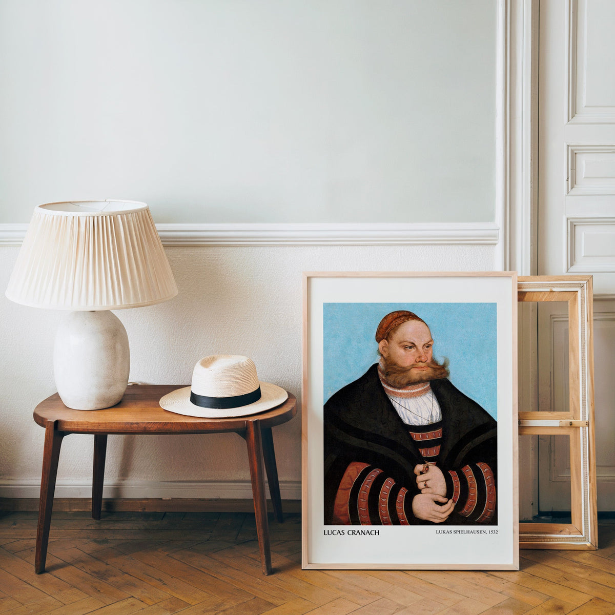 Old masters poster in a light wood frame leaning by a bench and hat