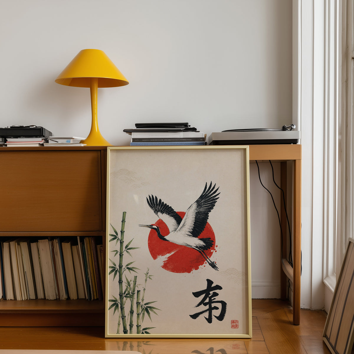 Crane bamboo red sun poster shown in a gold frame leaning under a teak desk with a yellow lamp