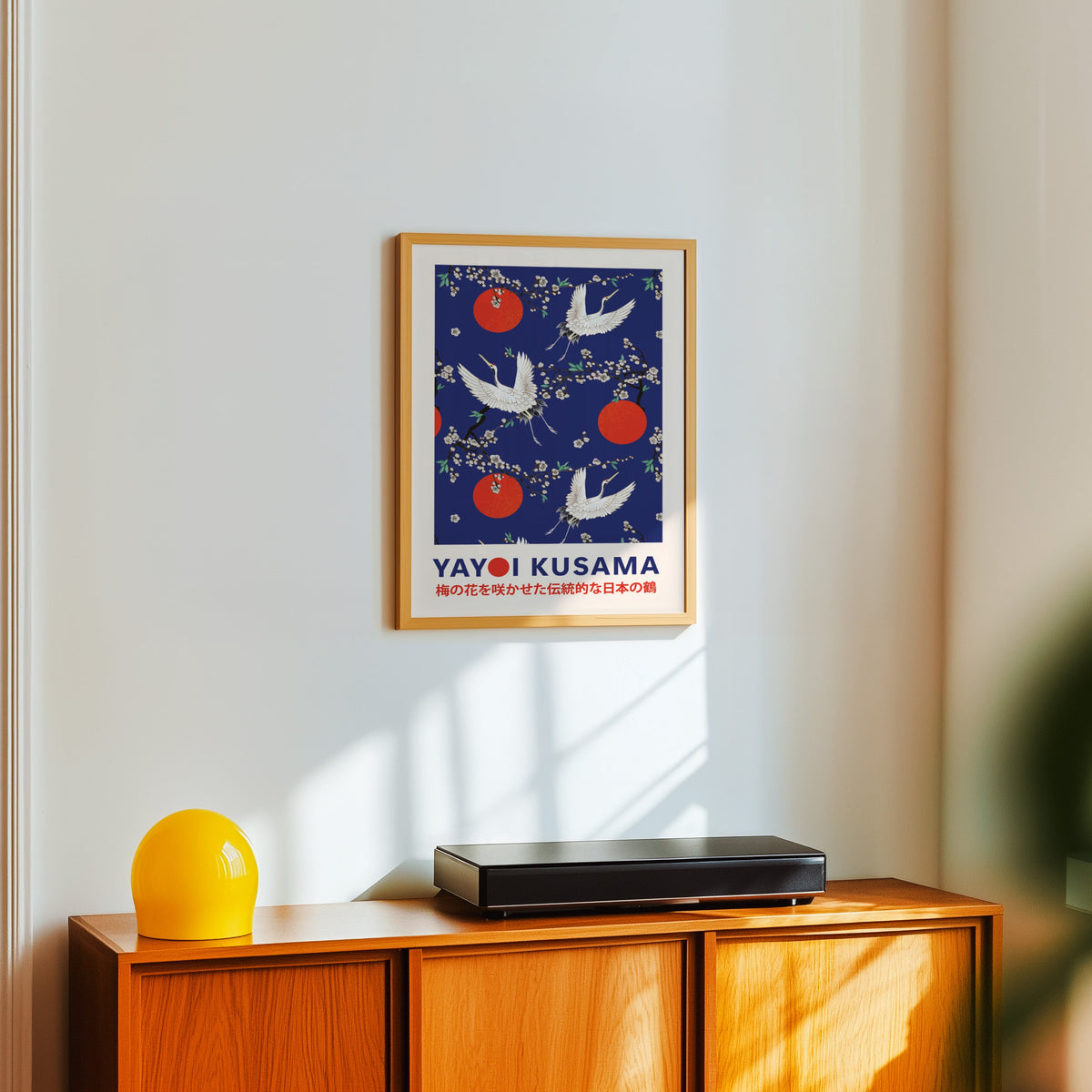 Yayoi Kusama inspired cranes and plum blossom on cobalt print in an oak frame over a teak sideboard with a yellow lamp