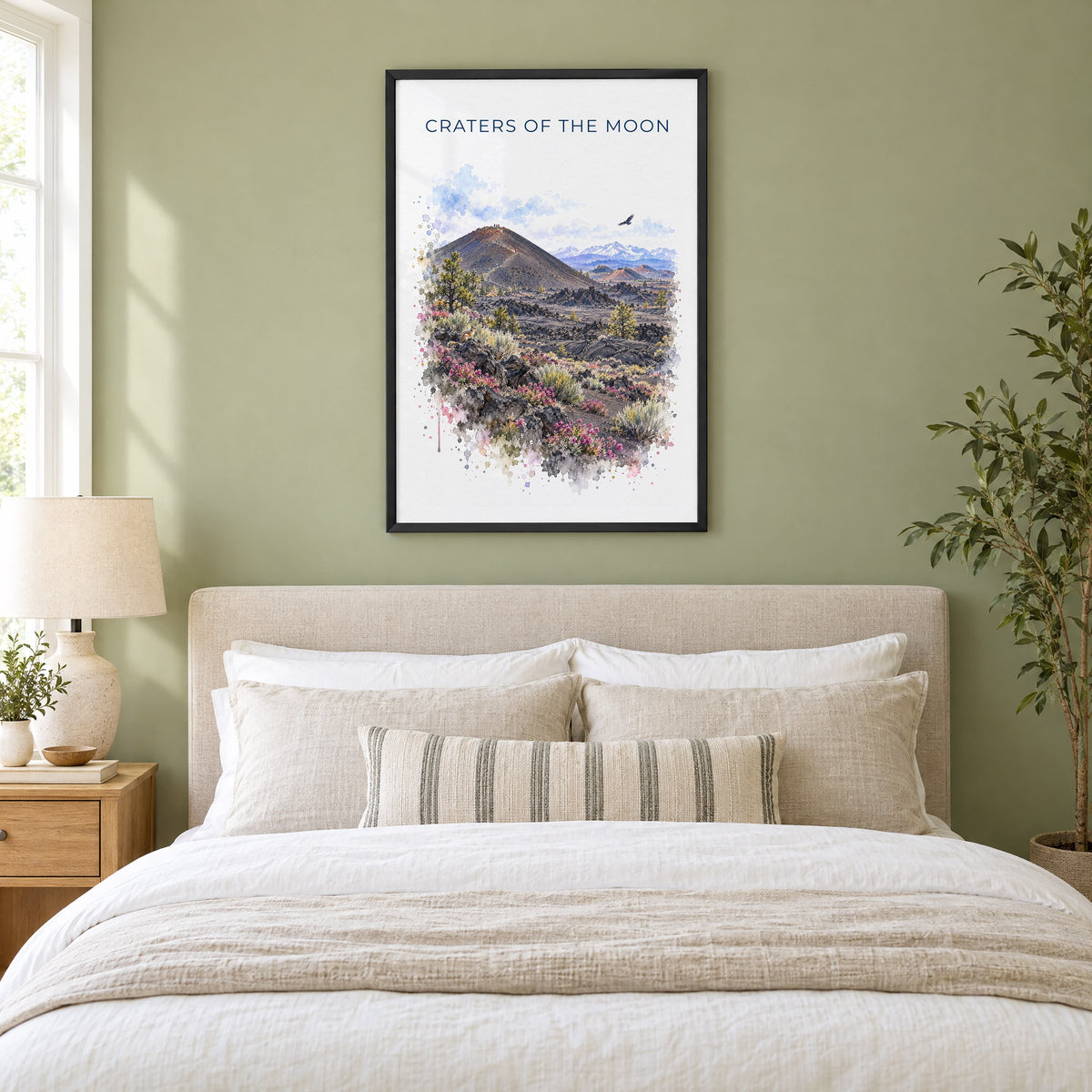 Craters of the Moon National Monument watercolor in a black frame above an upholstered headboard in a sage green bedroom
