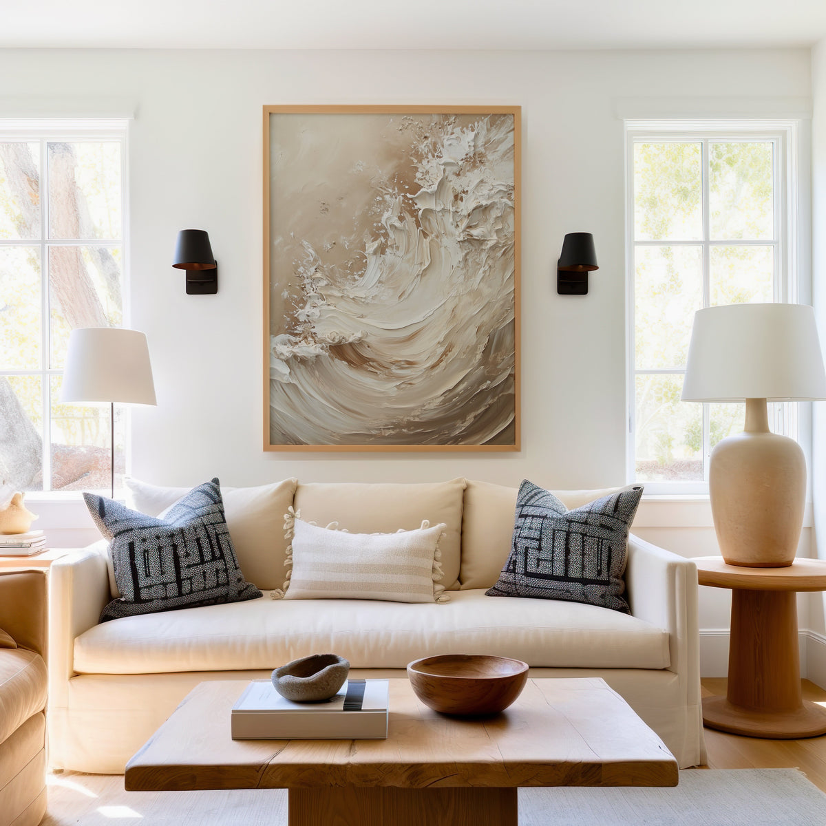 Cream and beige impasto wave abstract print in a light oak frame above a cream sofa between two black wall sconces