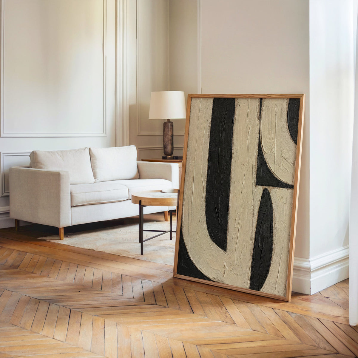 Cream and black U bands mid century abstract print in an oak frame leaning on a herringbone floor by a cream linen sofa
