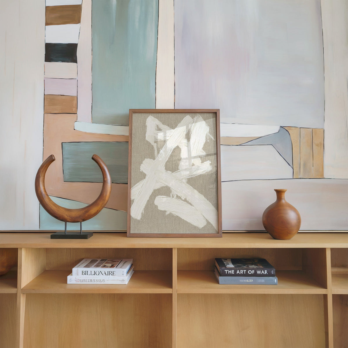 Cream impasto crossed strokes on linen print in a walnut frame on an oak shelf beside a wooden crescent sculpture