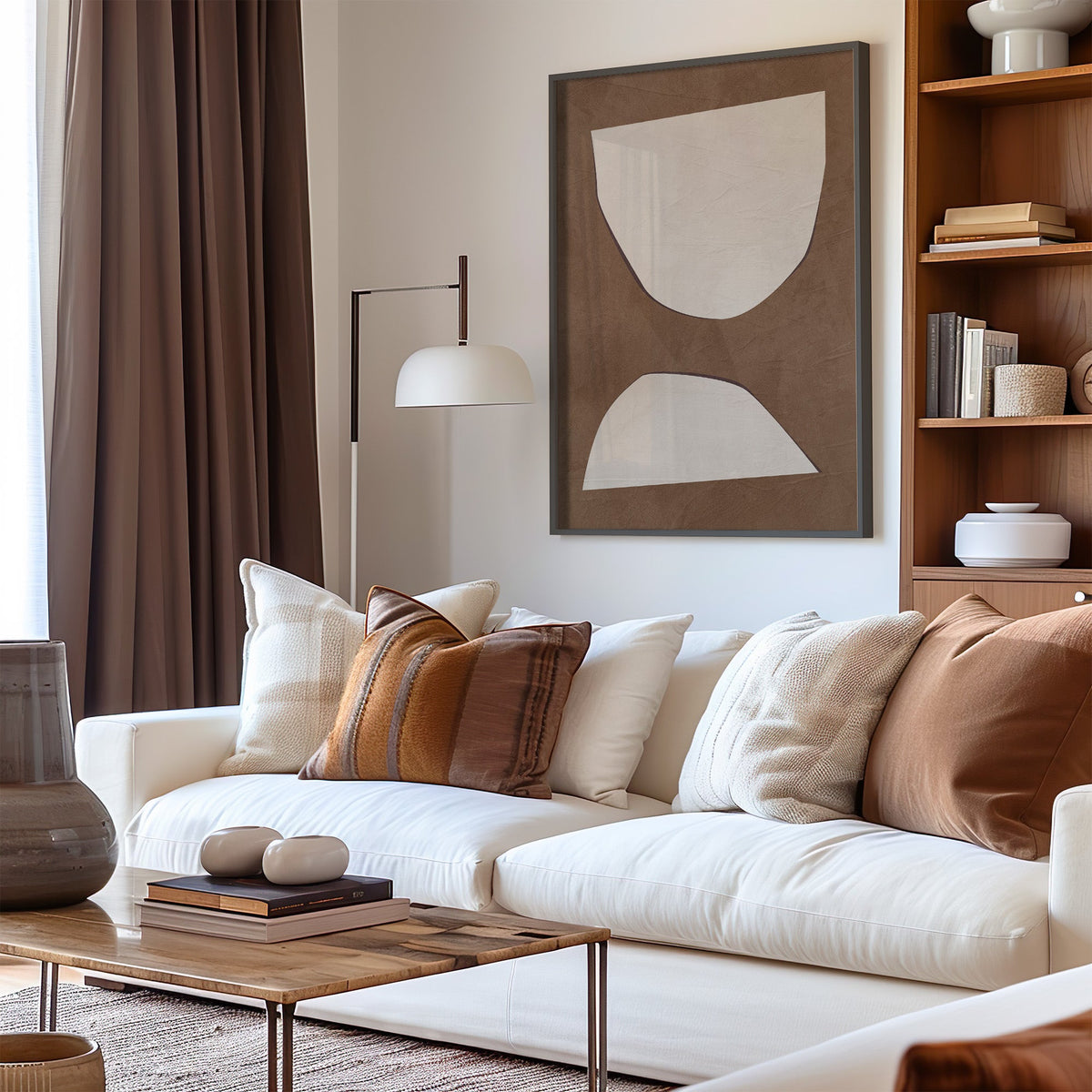 Cream paper cutout shapes on brown print in a black frame above a cream sofa with brown striped pillows