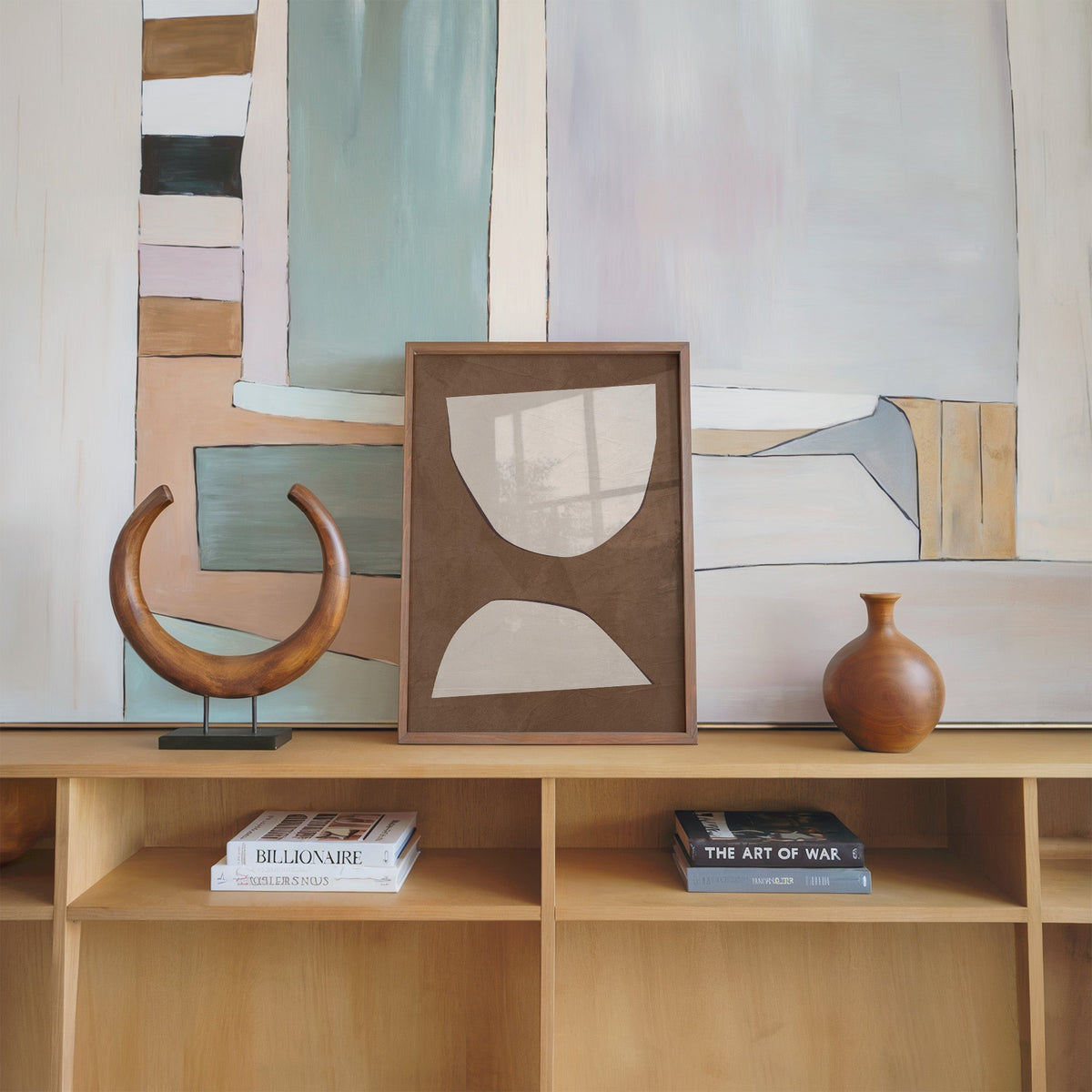 Cream paper cutout shapes on brown print in a walnut frame on an oak shelf beside a wooden crescent sculpture