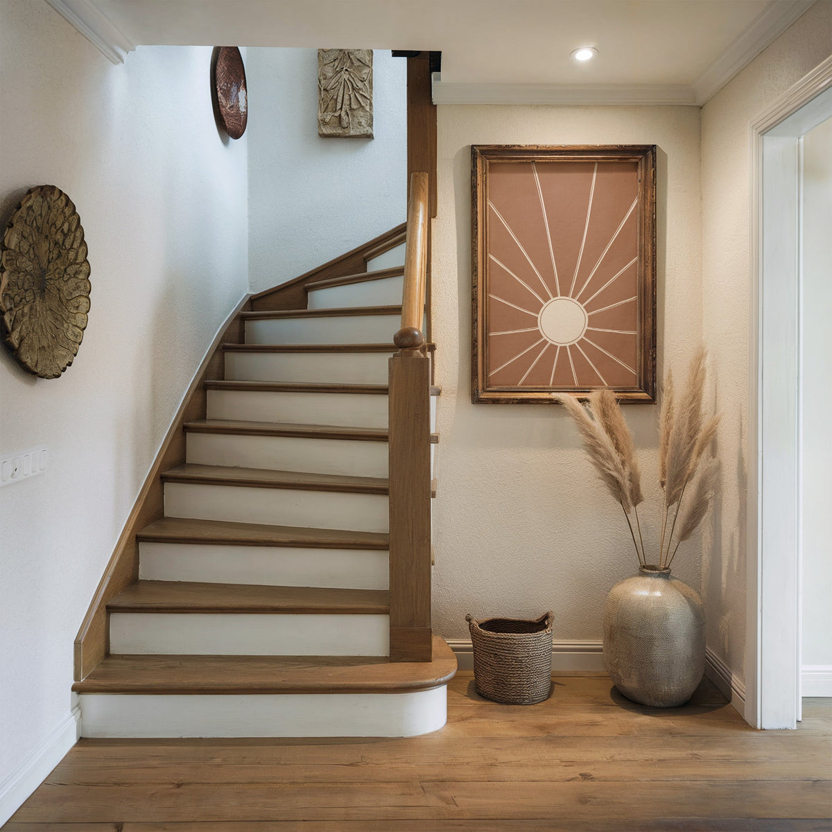 Cream sunburst rays on terracotta boho print shown in a rustic wood frame in a hallway beside a wooden staircase