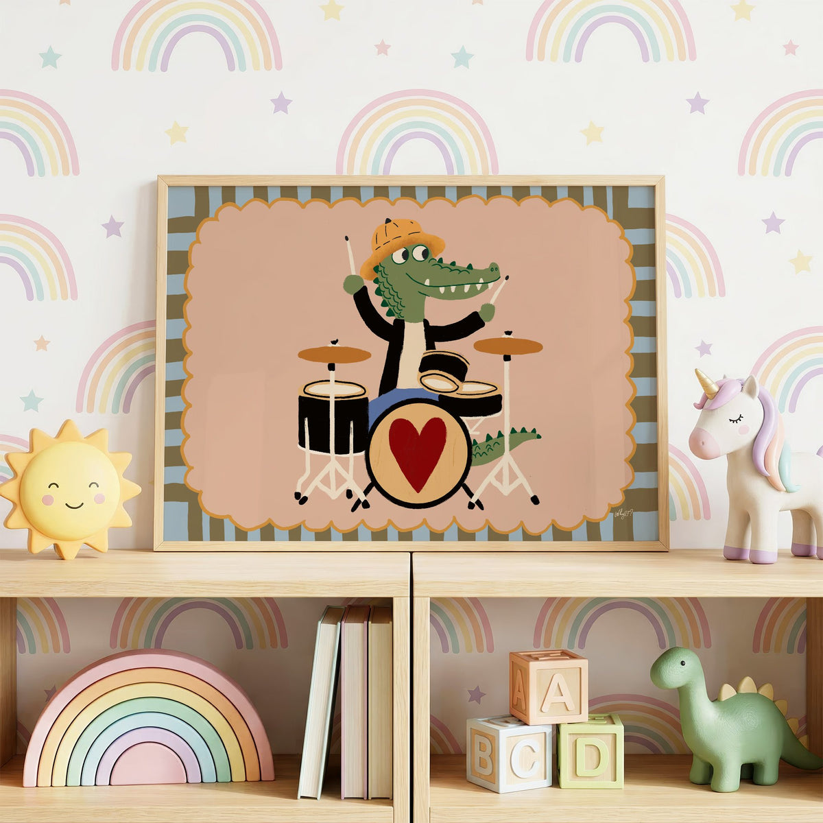 Crocodile playing heart drum kit nursery print in an oak frame on a toy shelf against rainbow wallpaper