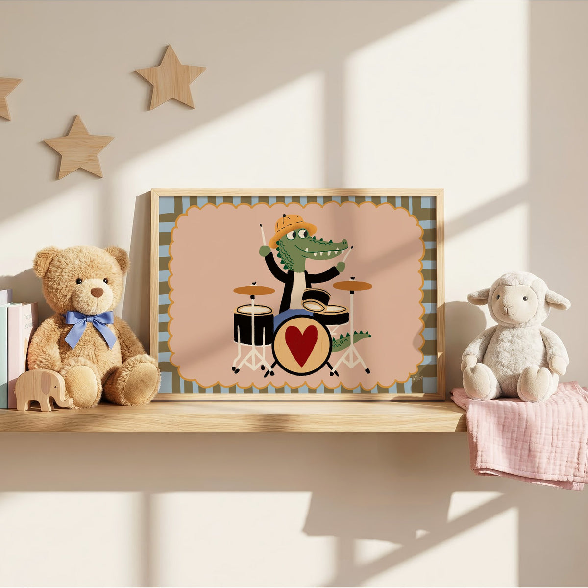 Crocodile playing heart drum kit nursery print in an oak frame on a wall shelf between a teddy bear and a toy lamb
