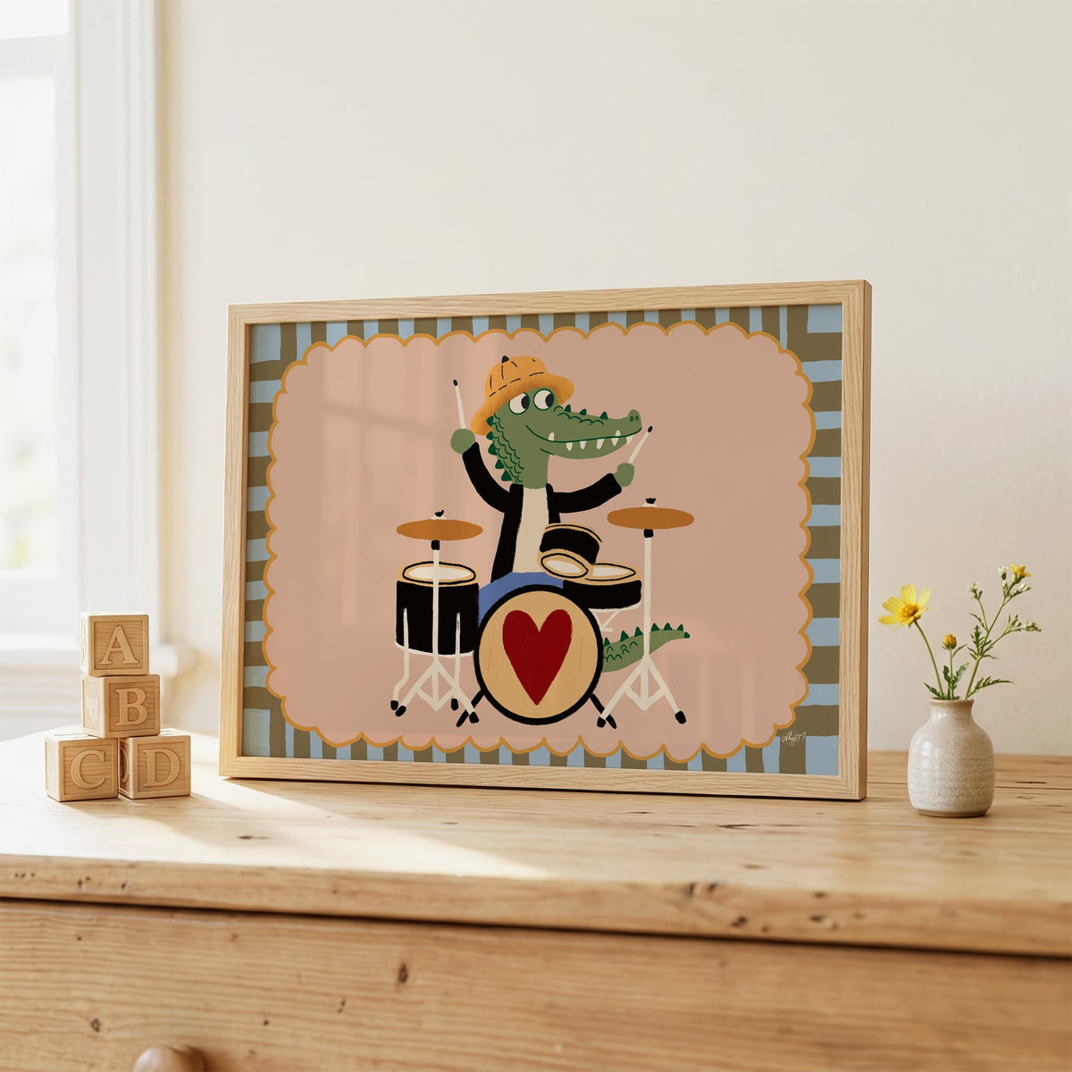 Crocodile playing heart drum kit nursery print in an oak frame on a wooden dresser beside ABC blocks