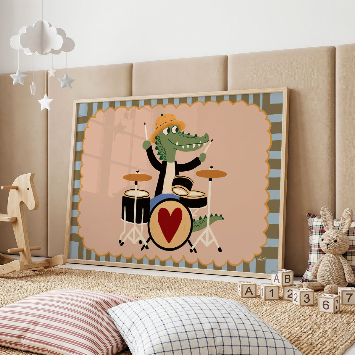 Crocodile playing heart drum kit nursery print in an oak frame on a padded wall by a wooden rocking horse