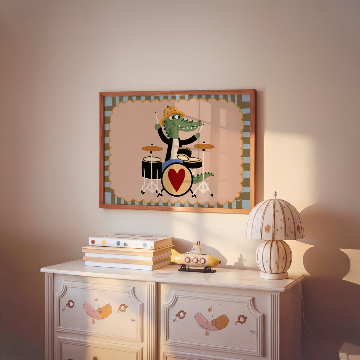 Crocodile playing heart drum kit nursery print in a cherry wood frame above a painted dresser and lamp