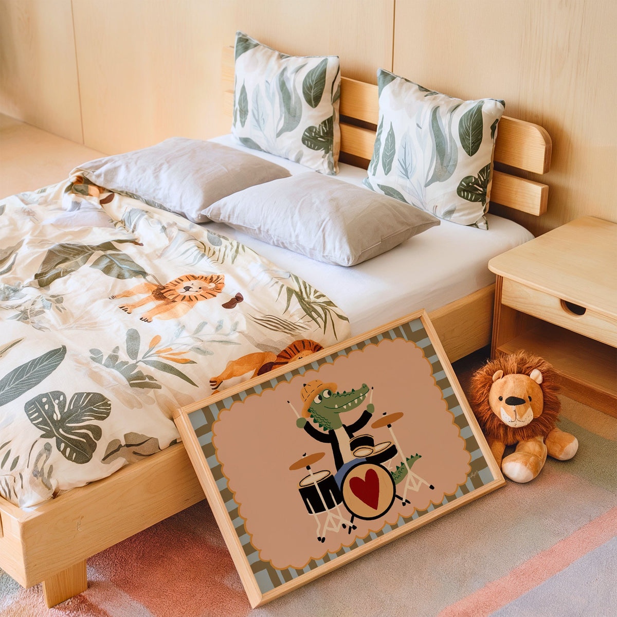 Crocodile playing heart drum kit nursery print in an oak frame leaning on a kids bed by a lion plush