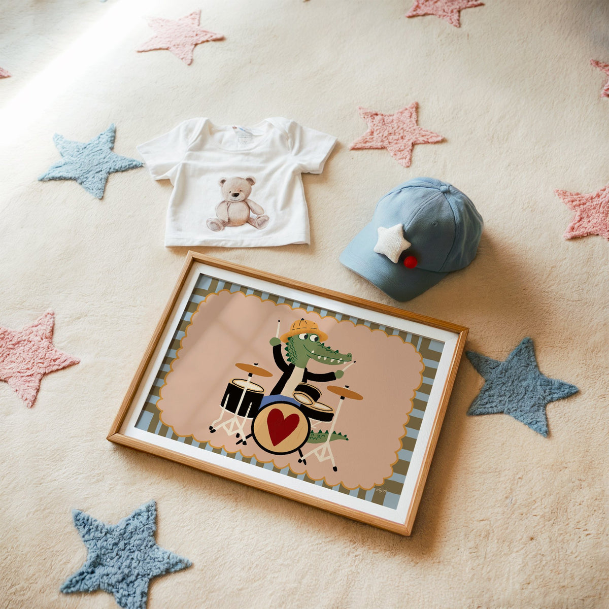 Crocodile playing heart drum kit nursery print in a matted oak frame on a star rug with a baby tee