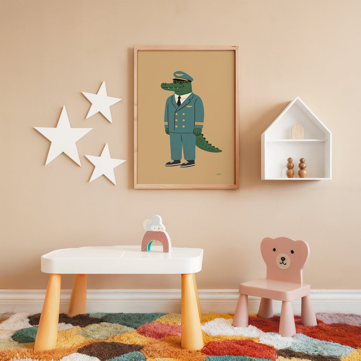 Crocodile in teal pilot uniform nursery print in an oak frame on a peach wall above a kids table with wall stars