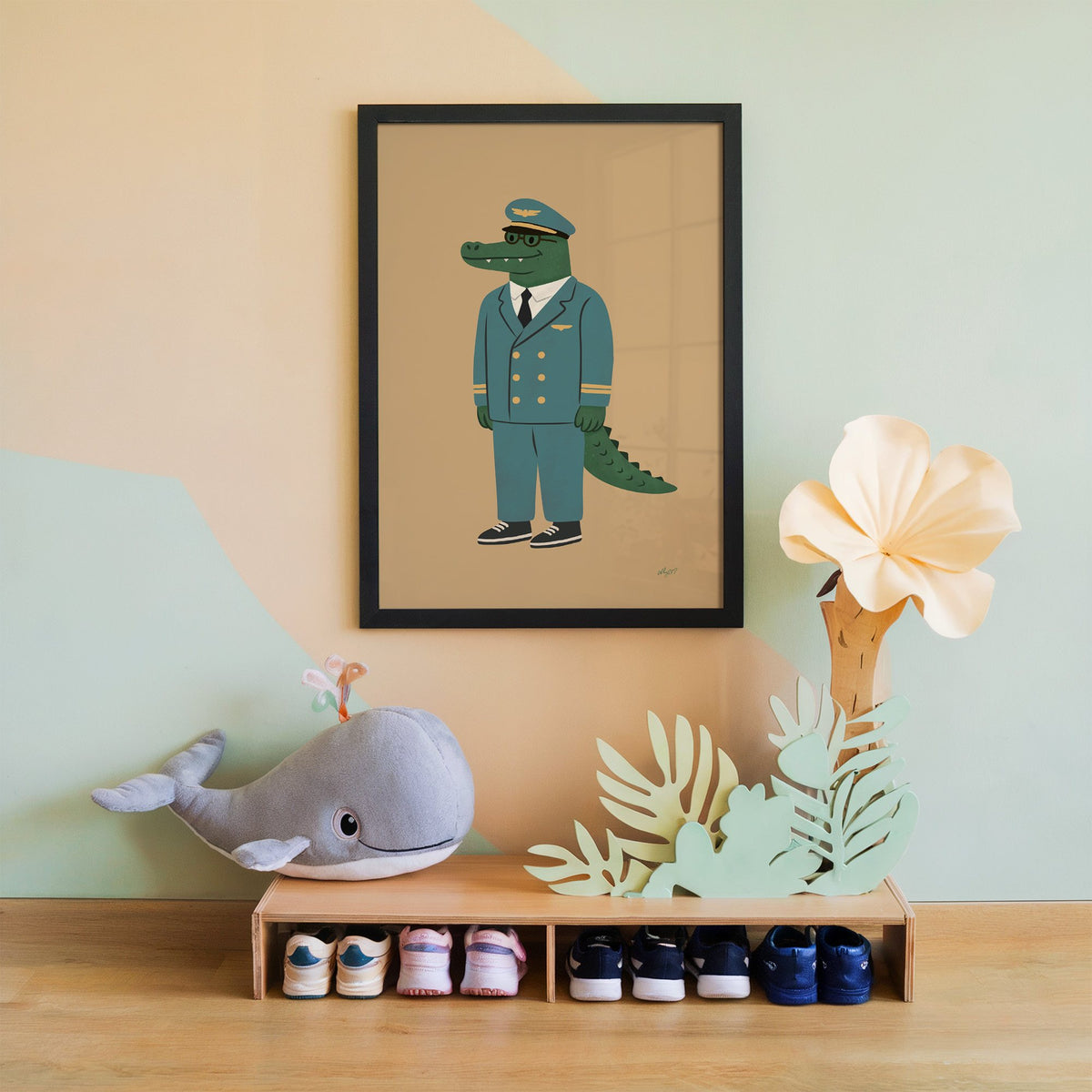 Crocodile in teal pilot uniform nursery print in a black frame on a mint and peach wall above a whale plush