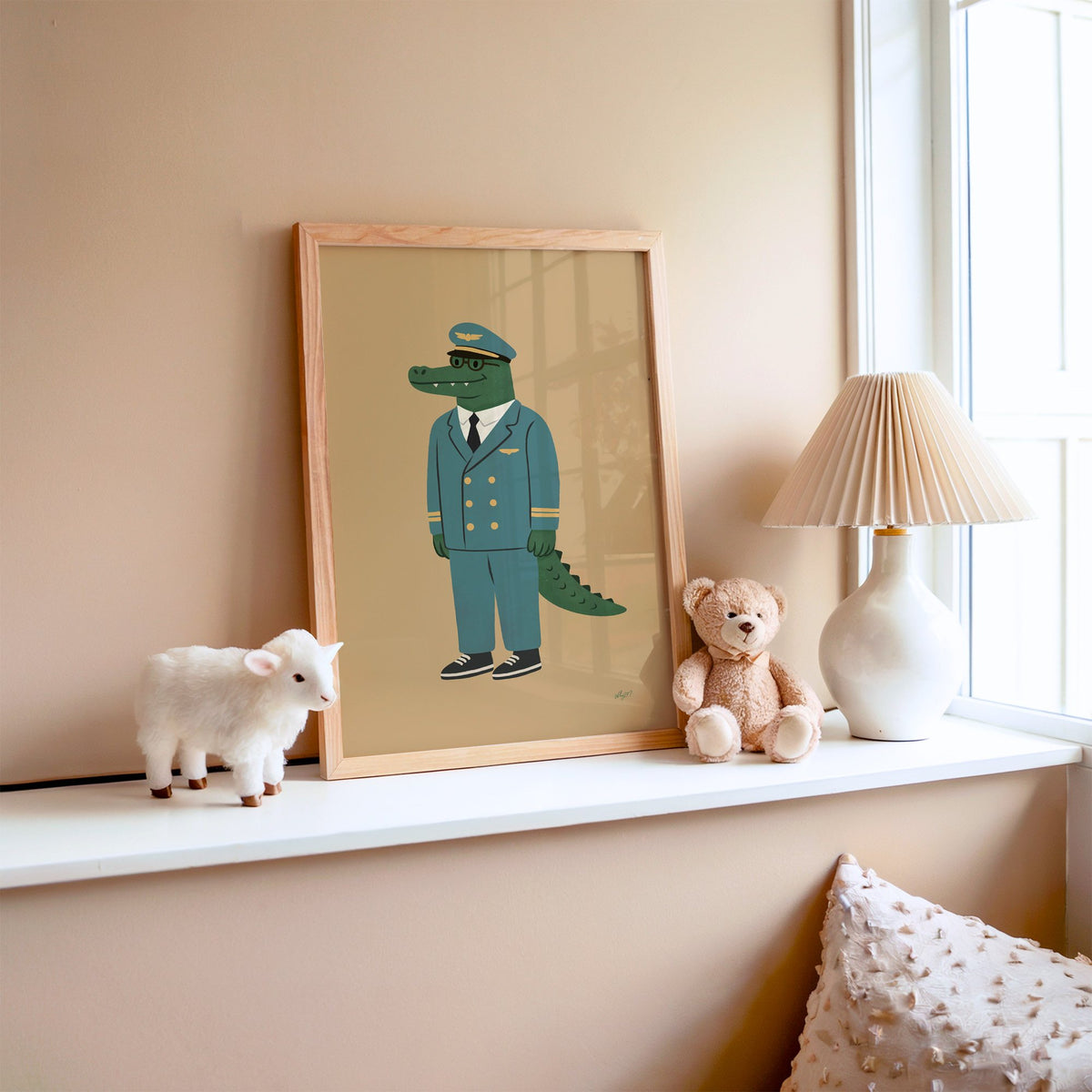Crocodile in teal pilot uniform nursery print in an oak frame on a window ledge with a toy lamb and teddy