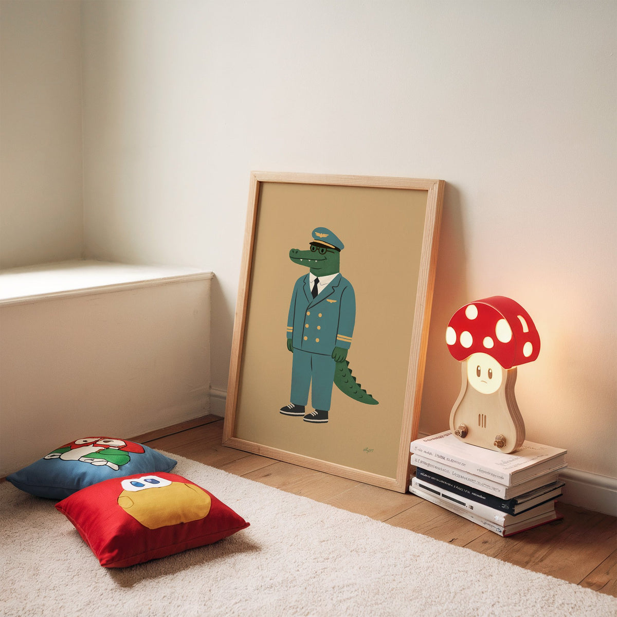 Crocodile in teal pilot uniform nursery print in an oak frame leaning on a rug beside a mushroom lamp and floor cushions