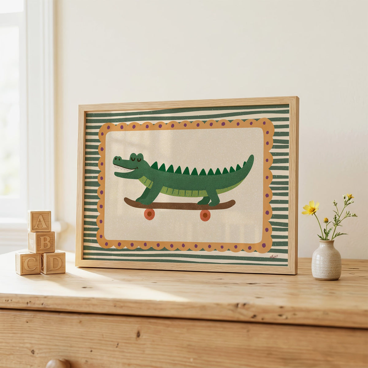 Smiling crocodile on skateboard nursery print in an oak frame on a wooden dresser beside ABC blocks