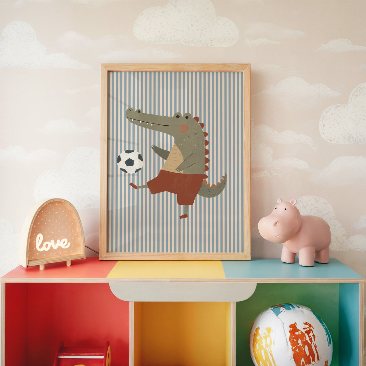 Crocodile soccer ball nursery print in an oak frame on a rainbow toy shelf against cloud wallpaper