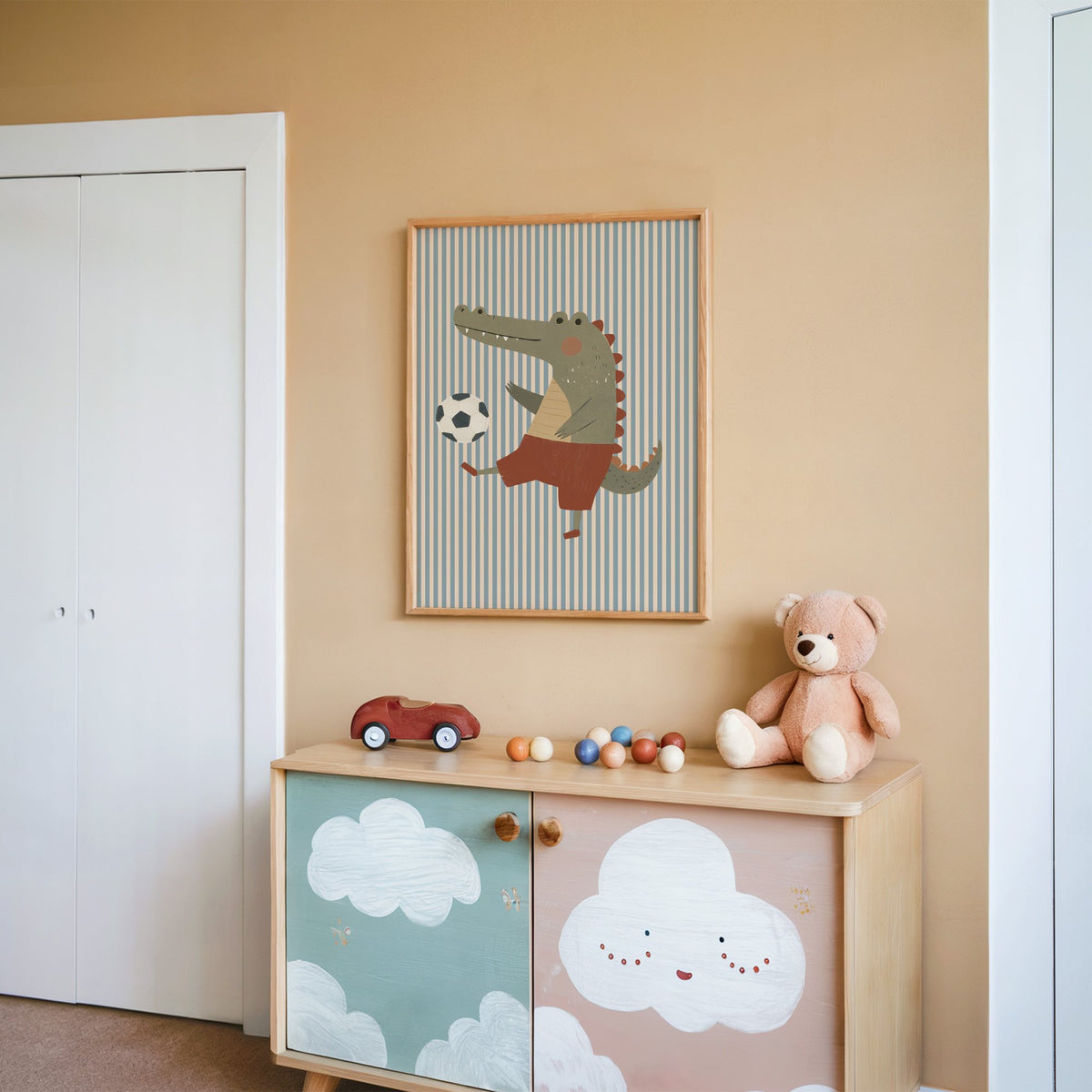 Crocodile soccer ball nursery print in an oak frame on a peach wall above a cloud-painted cabinet