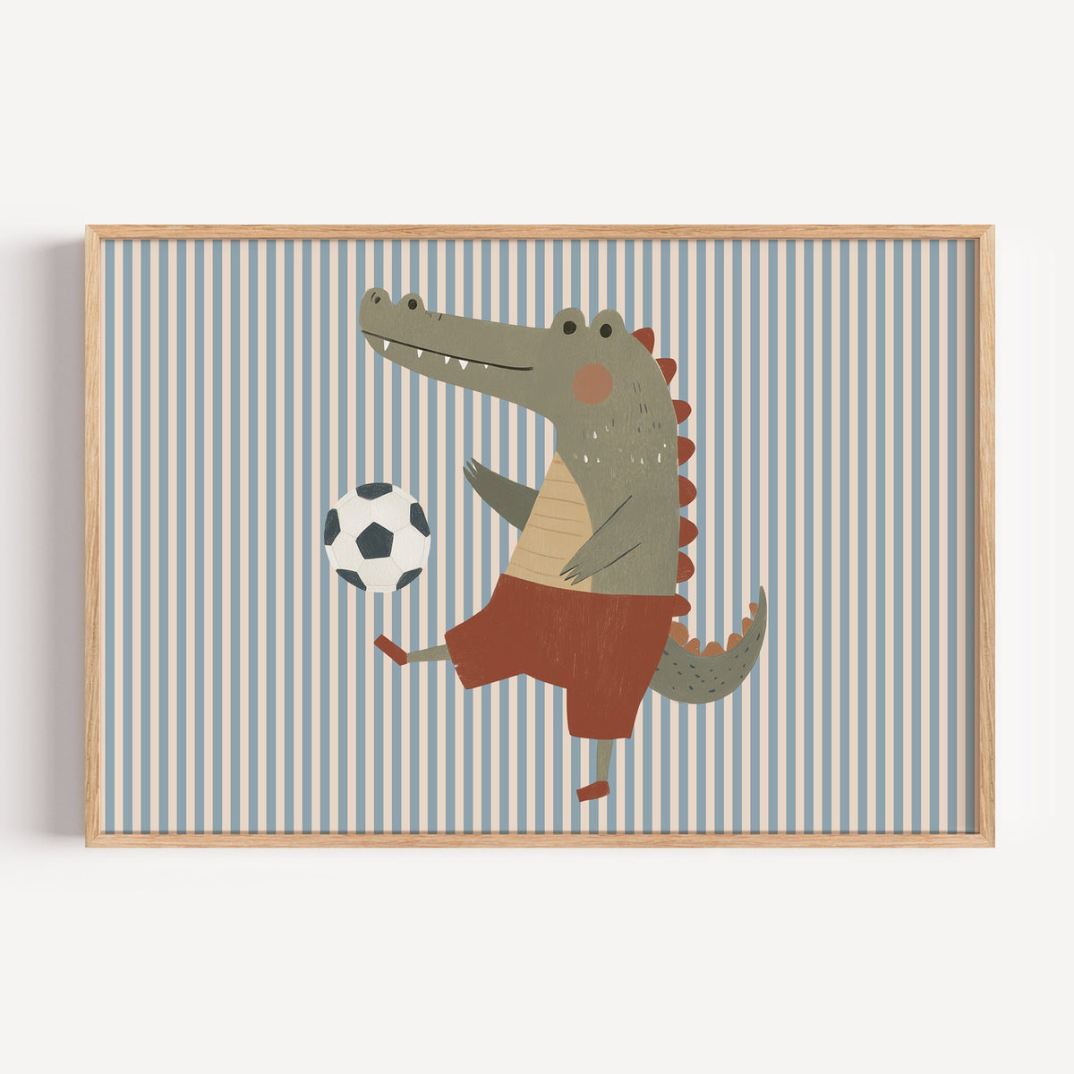 Landscape crocodile soccer ball nursery print in a light oak frame on a plain white wall