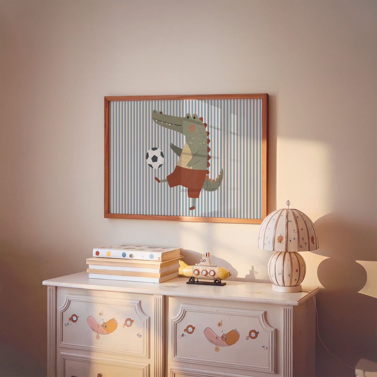 Landscape crocodile soccer ball nursery print in a cherry wood frame above a painted dresser and lamp