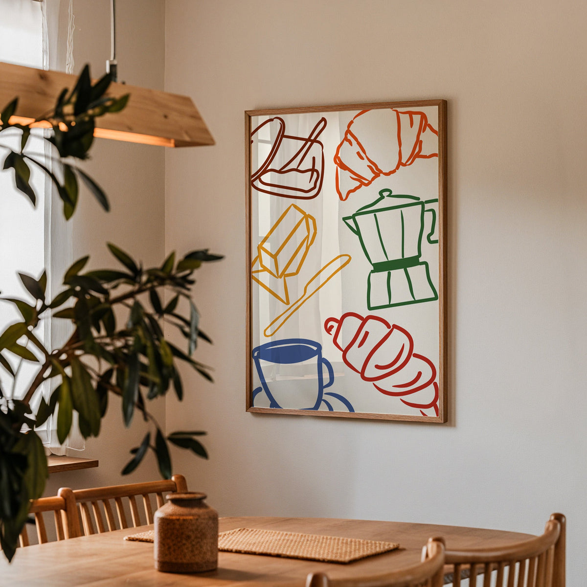 Croissant and coffee doodle print in a walnut frame above a dining table beside an olive tree