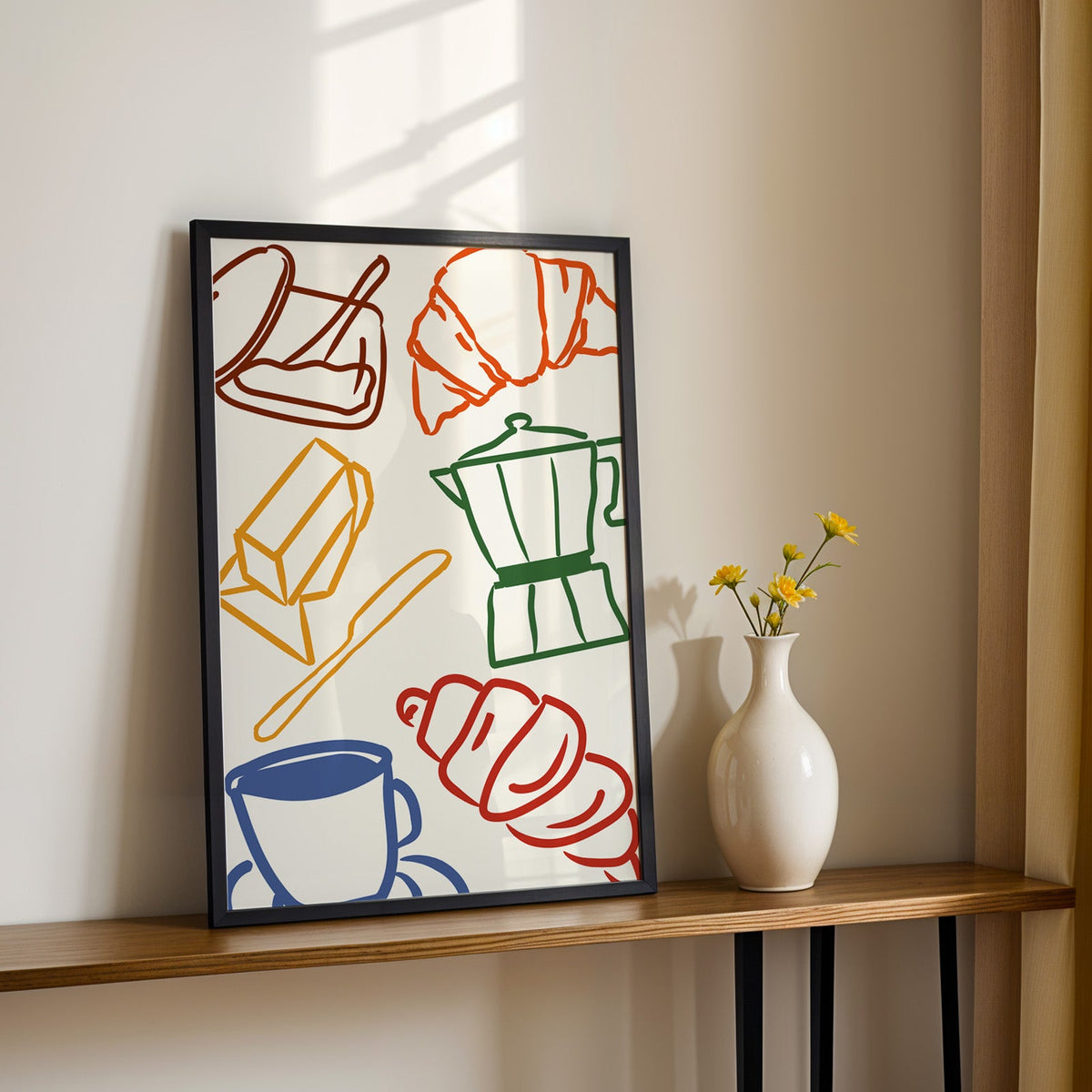 Croissant and coffee doodle print in a black frame on a console table with yellow daisies