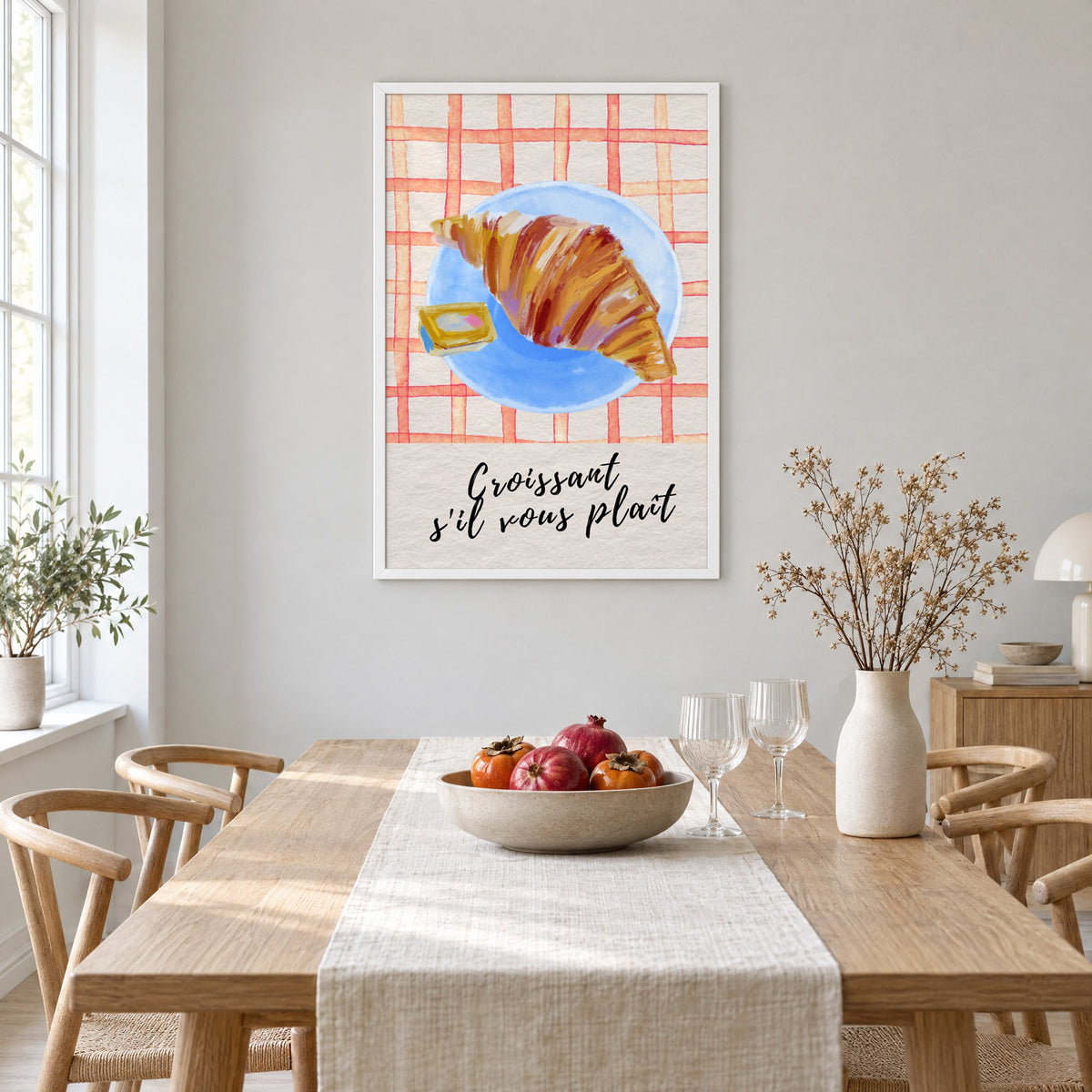 Croissant s'il vous plait blue plate print in a white frame above a light oak dining table with a linen runner and fruit bowl