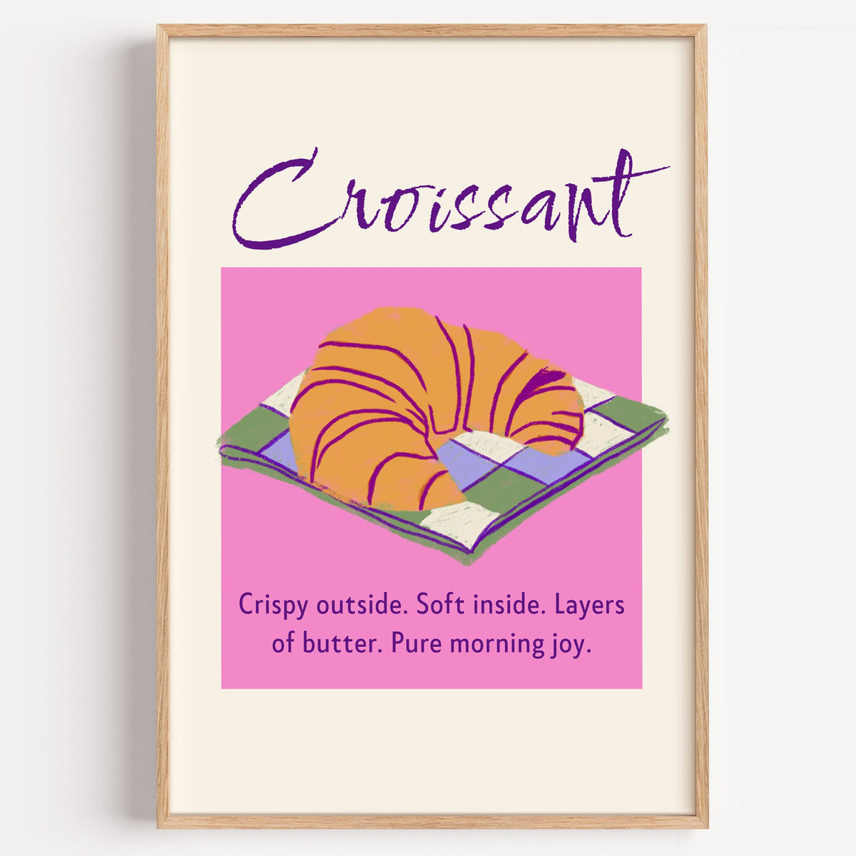 Croissant on checkered napkin pink panel print in a light oak frame on a plain white wall