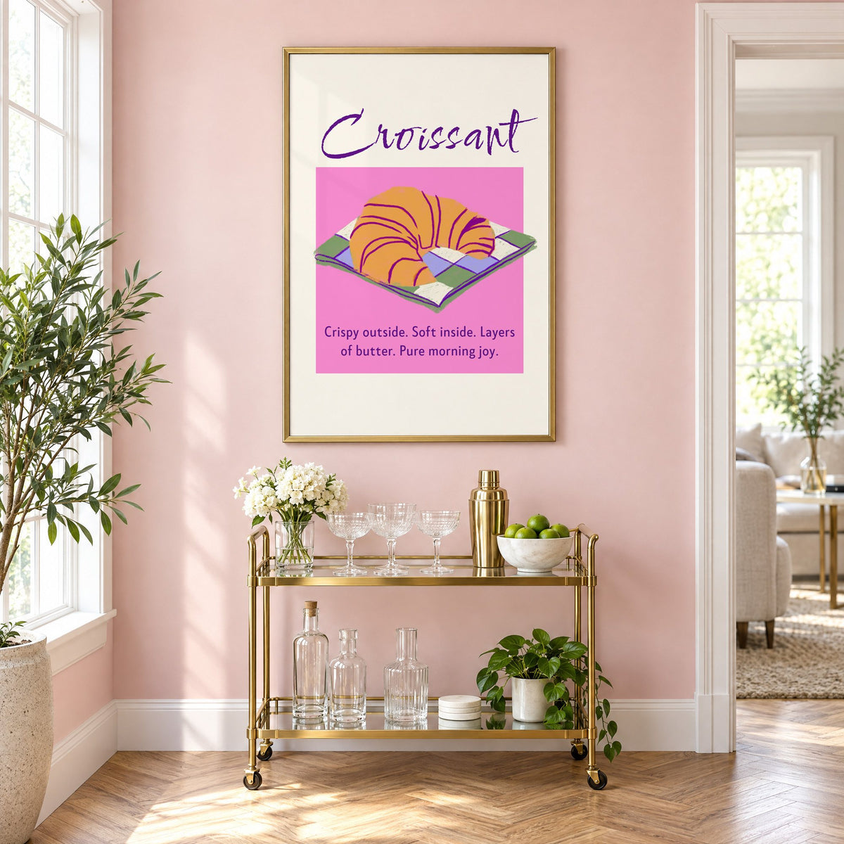 Croissant on checkered napkin pink panel print in a brass frame on a blush pink wall above a gold bar cart with glassware