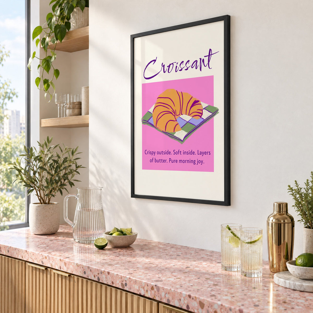 Croissant on checkered napkin pink panel print in a black frame above a pink terrazzo cocktail counter with limes, seen at an angle