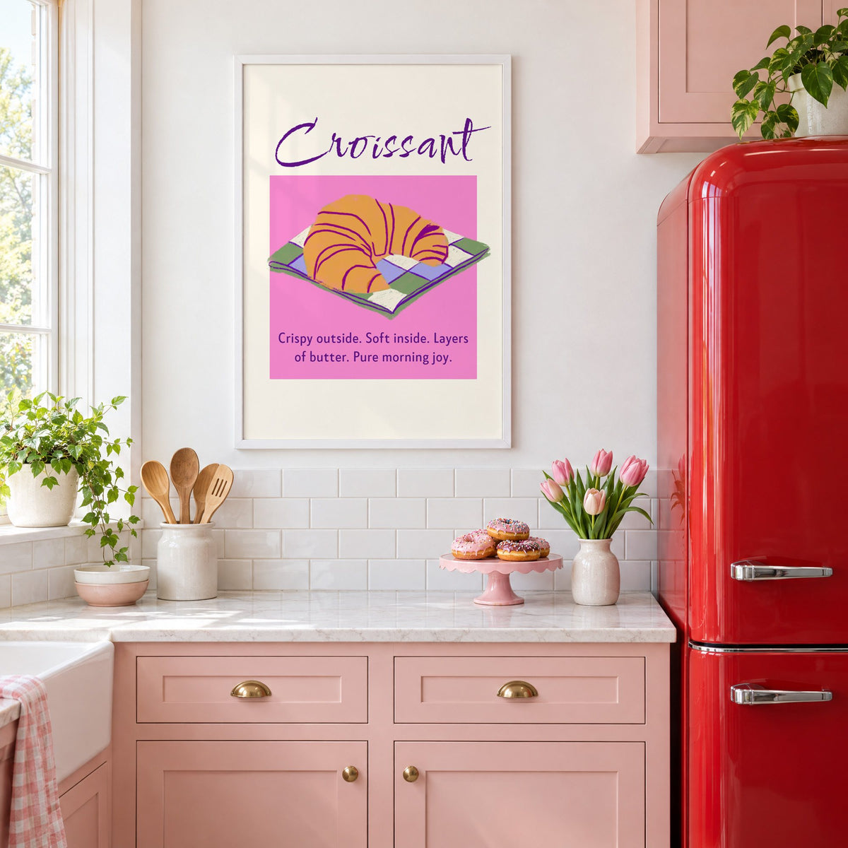 Croissant on checkered napkin pink panel print in a white frame above pink cabinets beside a red retro fridge
