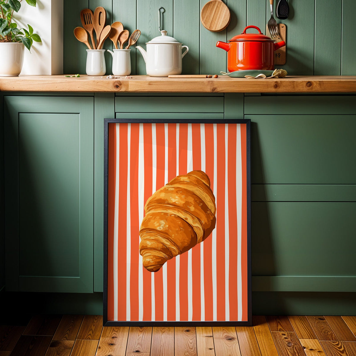 Painted croissant print in a black frame against sage green kitchen cabinets