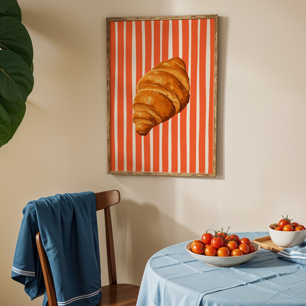 Painted croissant print in an oak frame above a blue linen table with ripe tomatoes