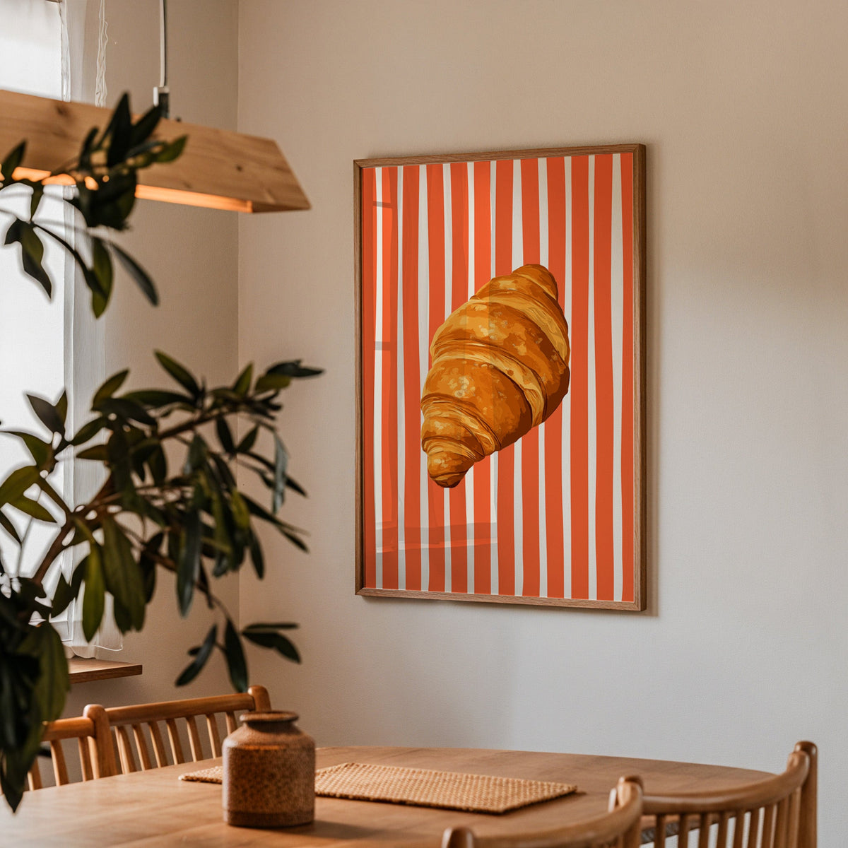 Painted croissant print in a walnut frame above a dining table beside an olive tree