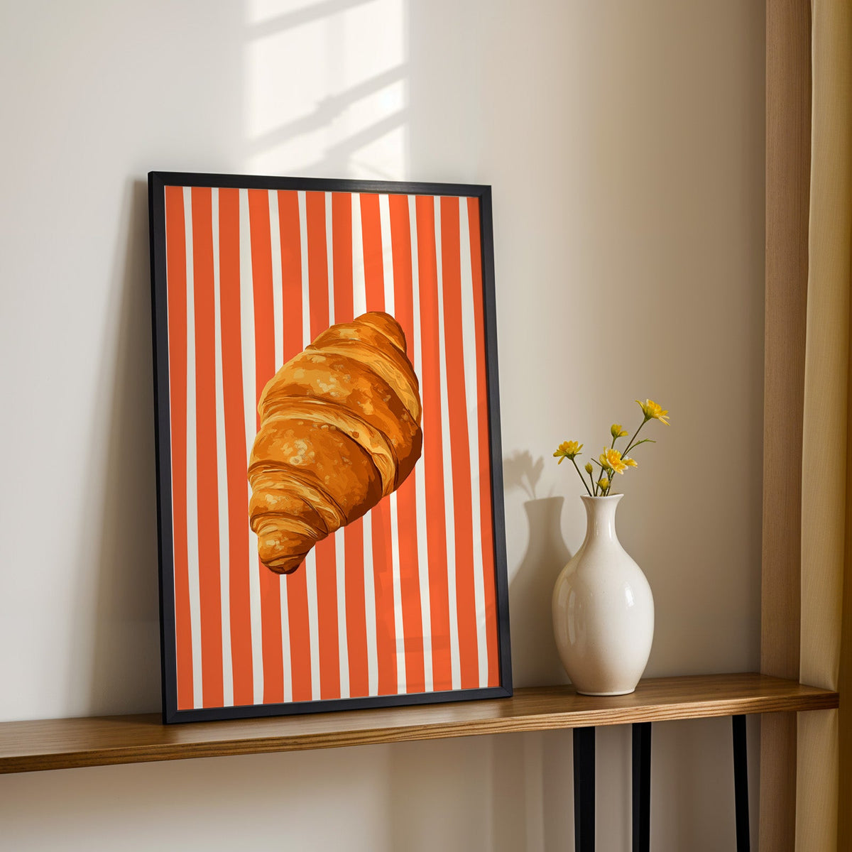 Painted croissant print in a black frame on a console table with yellow daisies