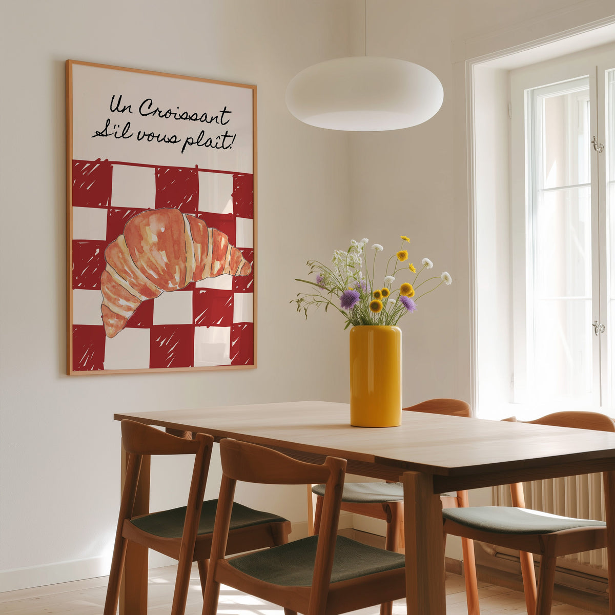 Un Croissant red check print in a slim oak frame above a wooden dining table under a round pendant light