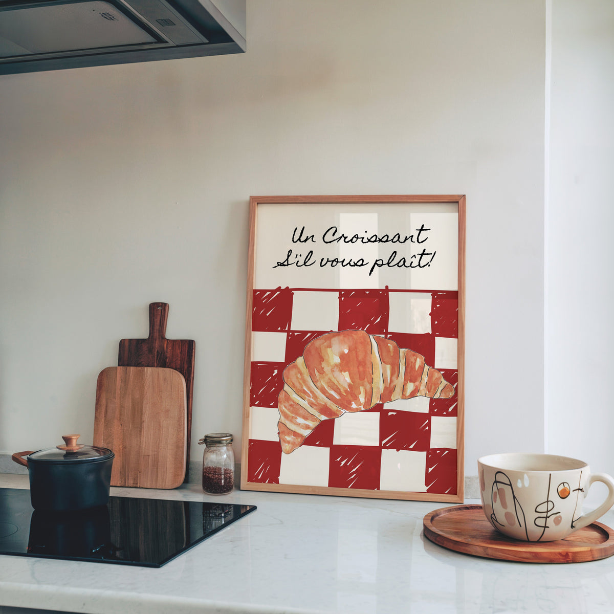 Un Croissant red check print in a pine frame leaning on a marble kitchen counter beside chopping boards