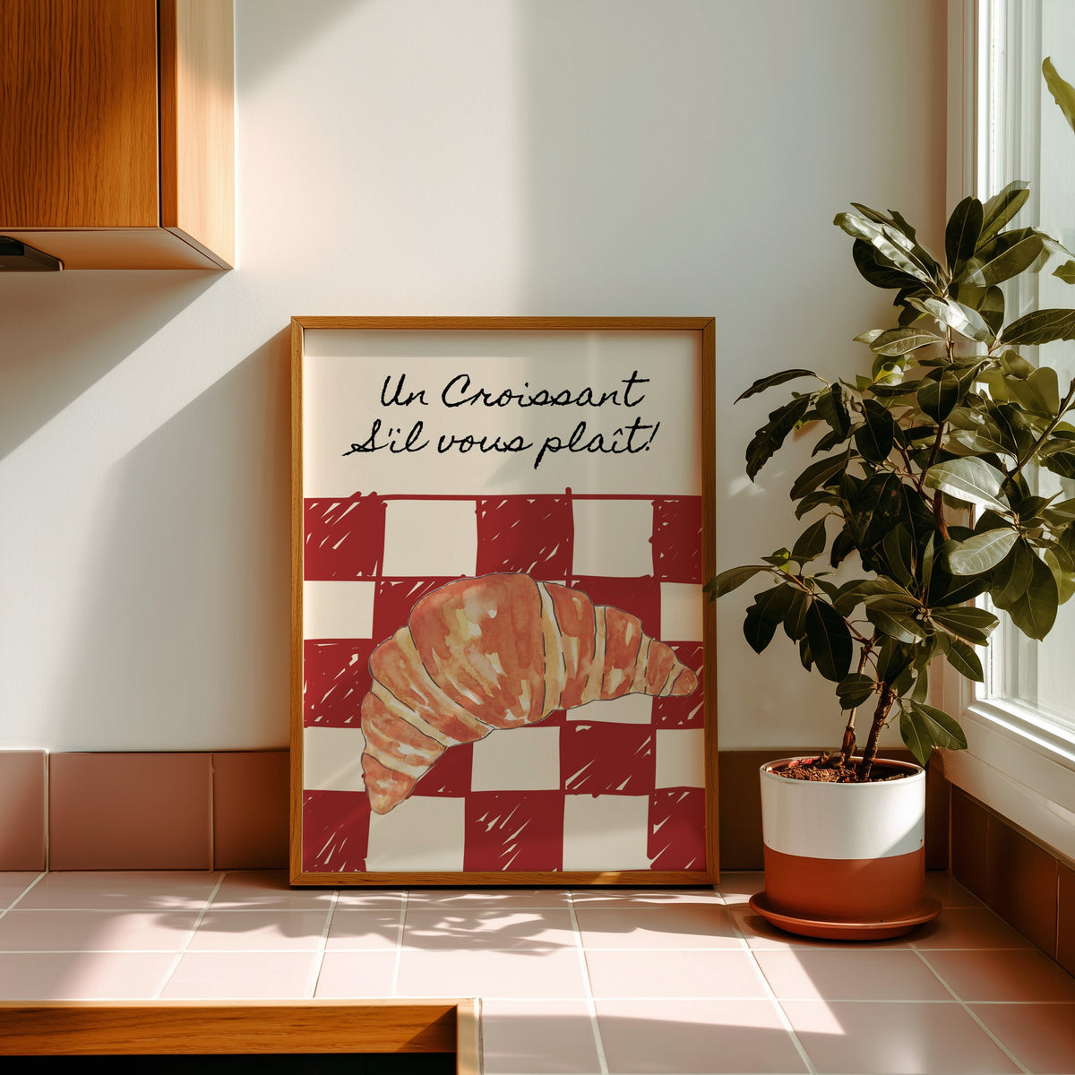 Un Croissant red check print in a golden oak frame leaning on a pink tiled ledge in strong afternoon sun