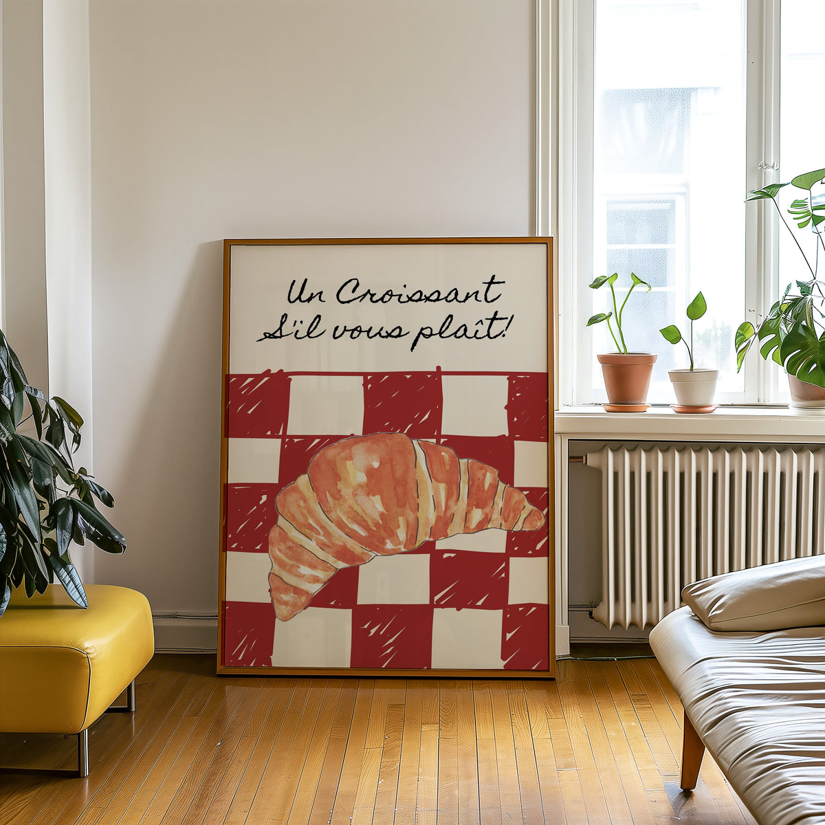 Un Croissant red check print in an oak frame leaning on a wooden floor beside a yellow leather bench